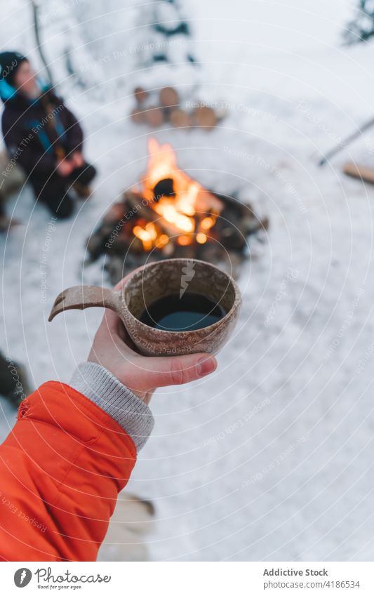 Unrecognizable woman drinking hot beverage near campfire on snowy winter day coffee hot drink bonfire campsite trip vacation child female traveler clay cup