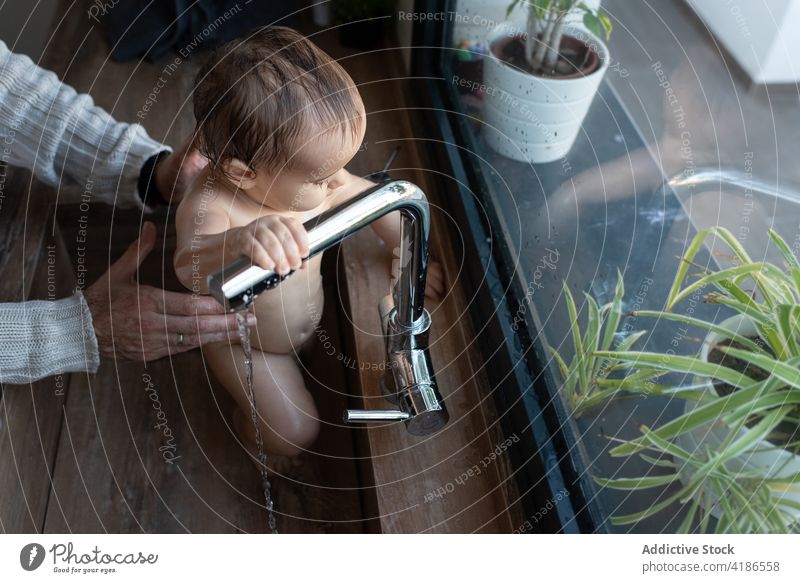 Crop father bathing baby in sink at home wash adorable delight play water kitchen toddler naked parent man together parenthood fatherhood happy cheerful playful
