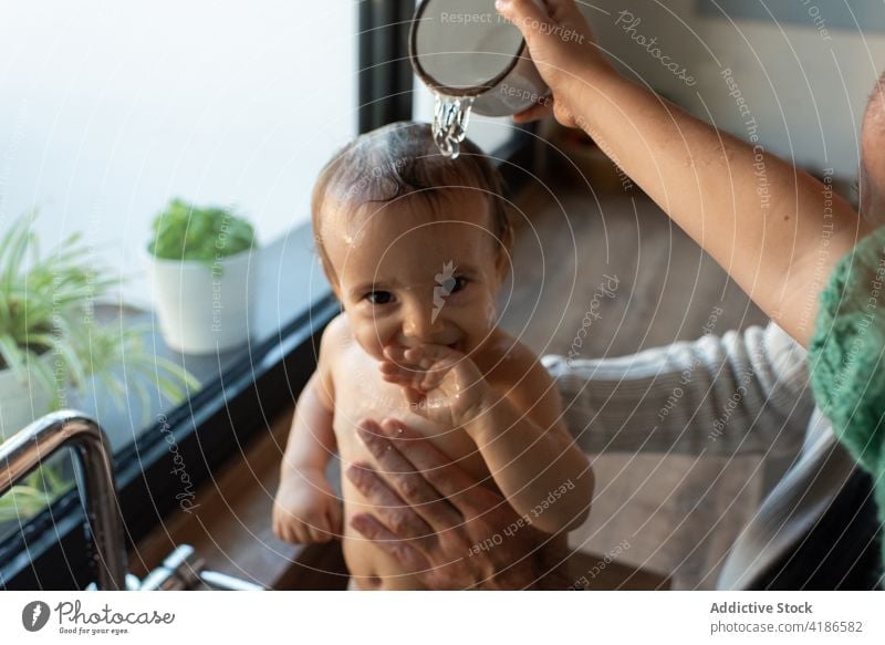 Parents bathing baby in sink wash parent water hygiene mother father smile toddler kitchen clean pour cute delight content together child family mom home kid