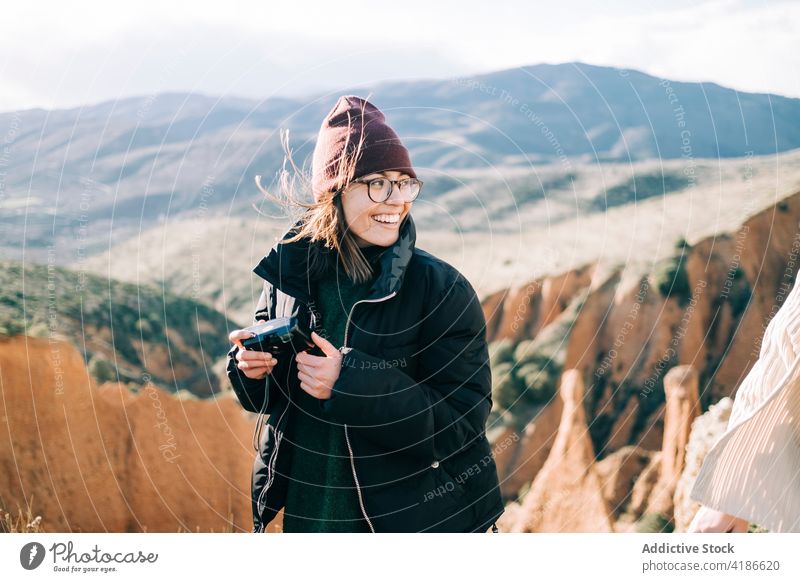Happy traveler with video camera near crop friend on canyon cheerful mount vacation woman highland nature smile device professional eyeglasses partner gorge