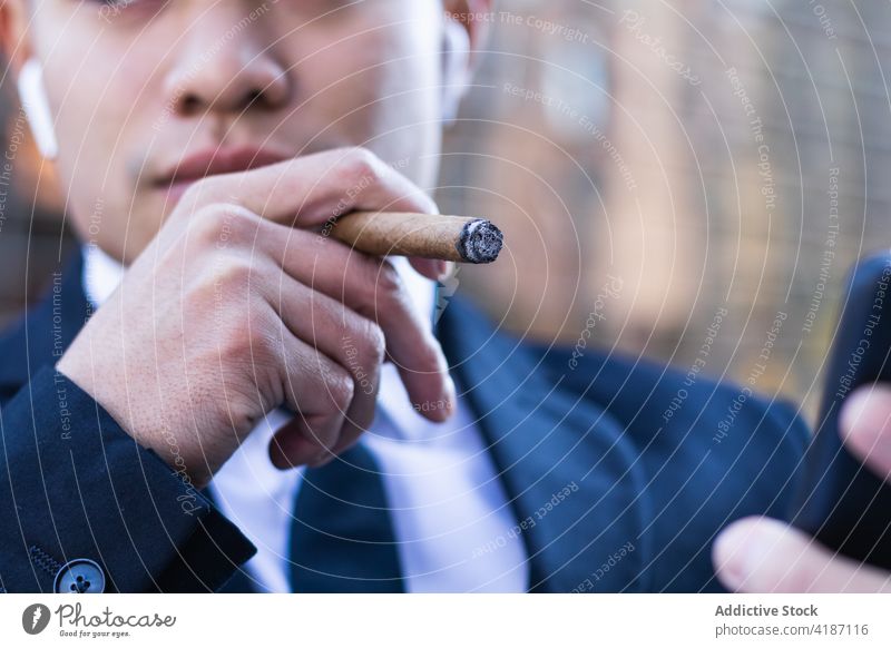 Businessman smoking cigar in street cafe businessman smoke entrepreneur browsing smartphone rich wealth using male asian ethnic table confident internet