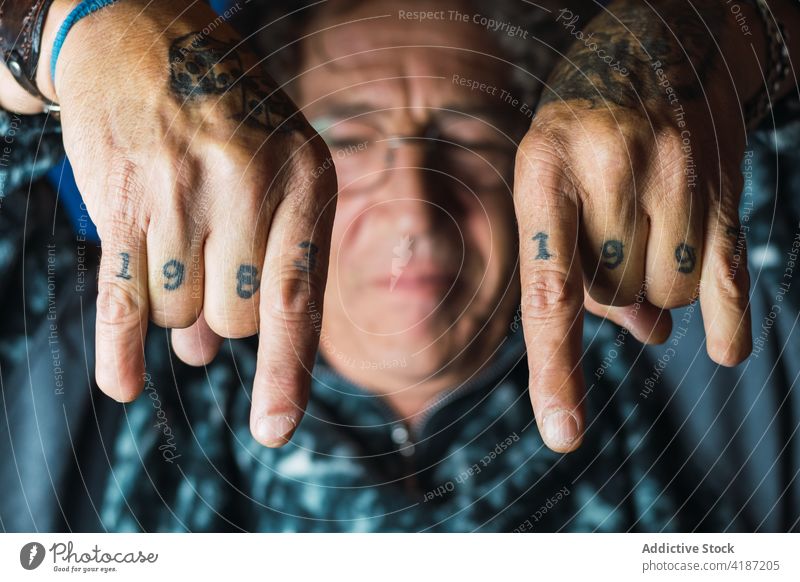 Positive tattooed mature man showing rock and roll gesture in studio informal positive joy rebel male middle age no thumb trendy curly hair eyeglasses content