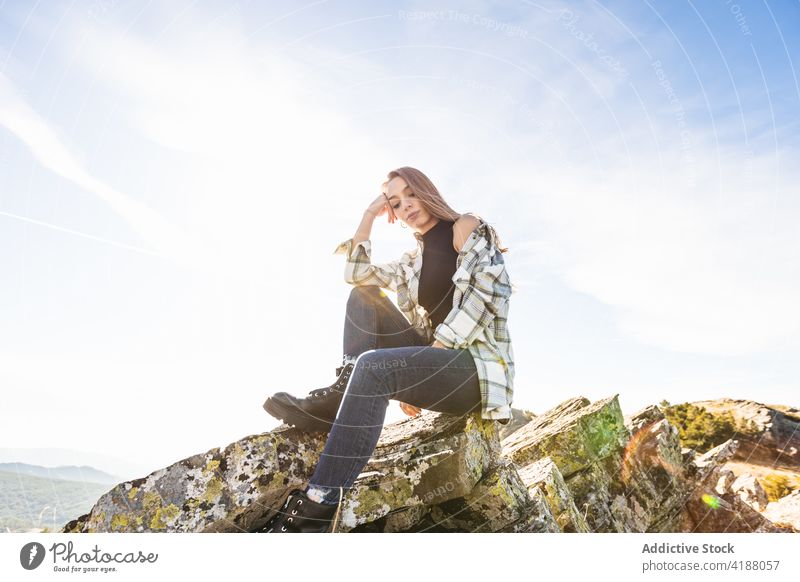 Wistful tourist resting on mountain under cloudy sky in sunlight lean on hand melancholy vacation trip woman moss boot casual wear ornament ponder wistful alone
