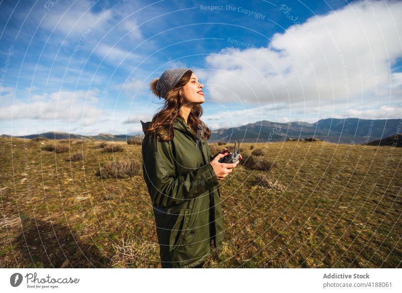 Traveler with drone controller on meadow under blue cloudy sky traveler remote uav pouting lips enjoy woman using trip device blue sky lawn vacation tourism