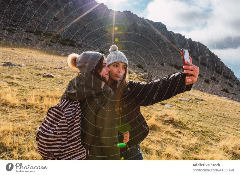 Female trekkers taking selfie with mobile phone in mountains on sunny day women share smartphone laugh interact vacation self-portrait nature photo using device