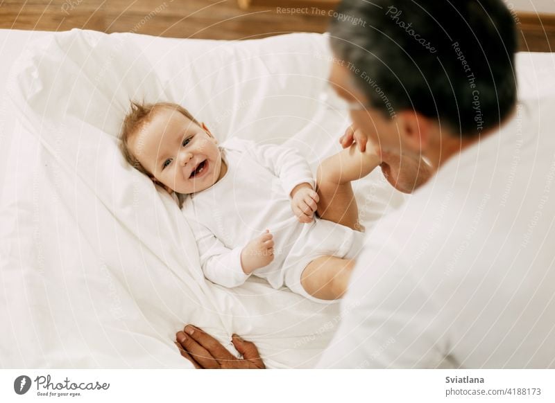 Happy father playing with adorable baby in the bedroom in a snow-white bed child dad parent cute love people man happiness home young kid person daughter face