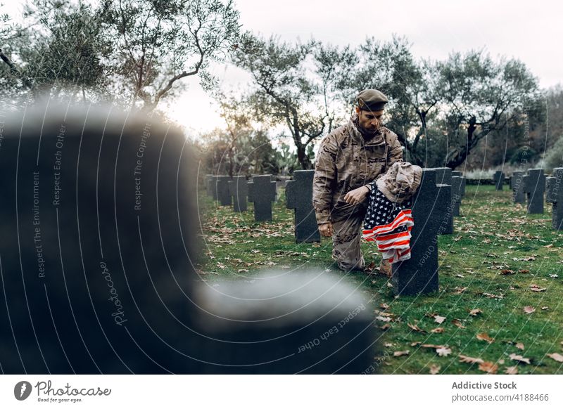 Soldier kneeling near graveyard in military cemetery man soldier sorrow hero rip memorial grief victim respect force army warrior ammunition camouflage outfit