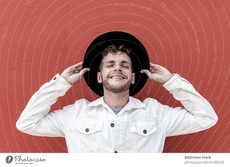 Happy young guy smiling with closed eyes against red background man smile eyes closed confident content style trendy personality adjust hat relax street happy