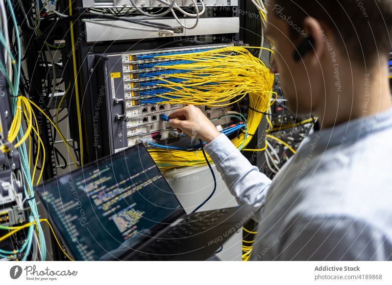 Male engineer controlling system in data center man assistant put cable using laptop network connection check male technology busy software job gadget internet