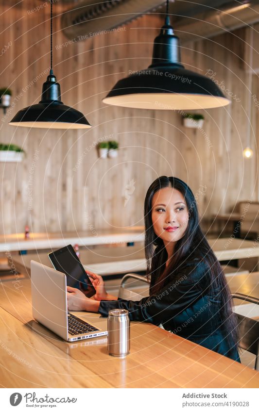 Asian businesswoman with gadgets working in cafe remote project content tablet laptop distance entrepreneur female asian ethnic device browsing smile