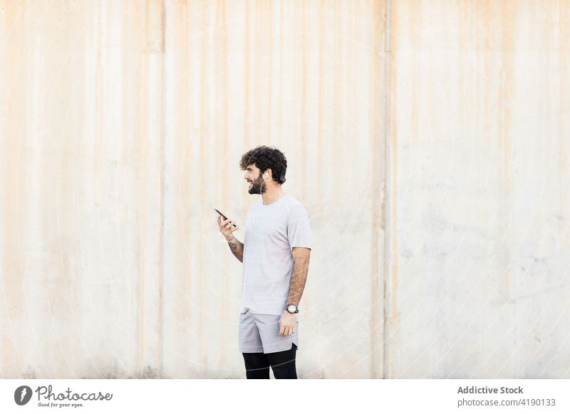 Smiling bearded sportsman with smartphone against wall masculine cheerful healthy lifestyle energy wellbeing macho vitality cellphone gadget device wellness