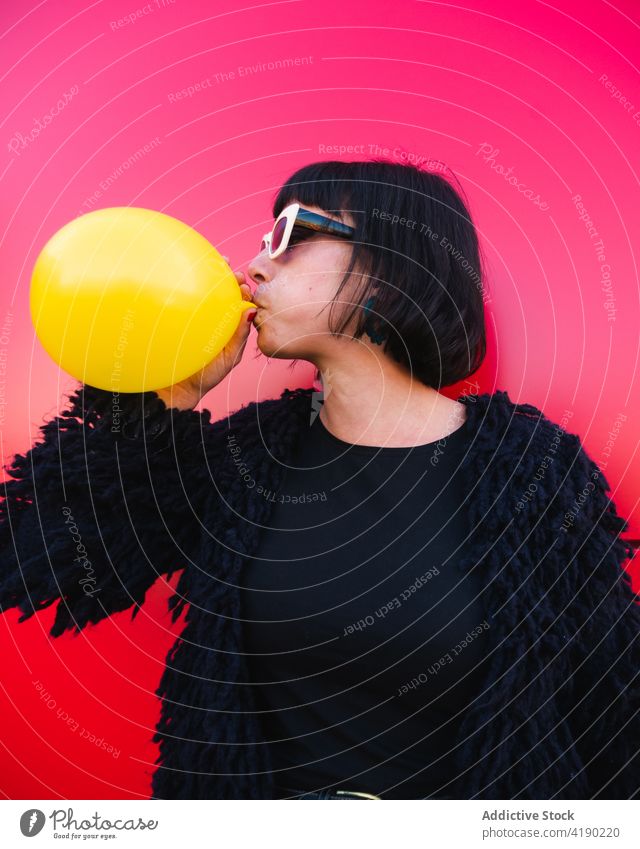 Trendy woman blowing balloon against red background air balloon fancy cool urban vivid trendy color female outfit fashion sunglasses street city style vibrant