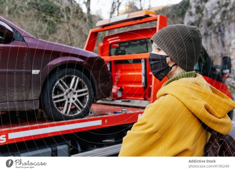 Woman in mask standing near car towed on truck woman breakdown outerwear coronavirus problem driver transport protect covid19 emotionless sad warm clothes
