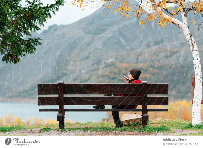 Woman sitting on bench in majestic autumn park woman admire talking smartphone mobile mountain lakeside rest enjoy picturesque severe peaceful ridge fall range