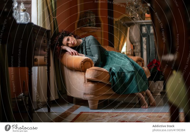 Calm woman in dress lying on armchair room vintage retro apartment flat interior old fashioned design female classic focus lady concentrate elegant home serious