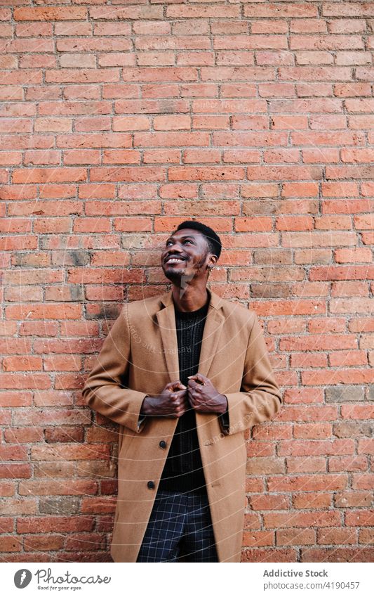 Stylish black man standing on brick wall on the street african american style modern trendy confident urban lifestyle exterior coat ethnic appearance city