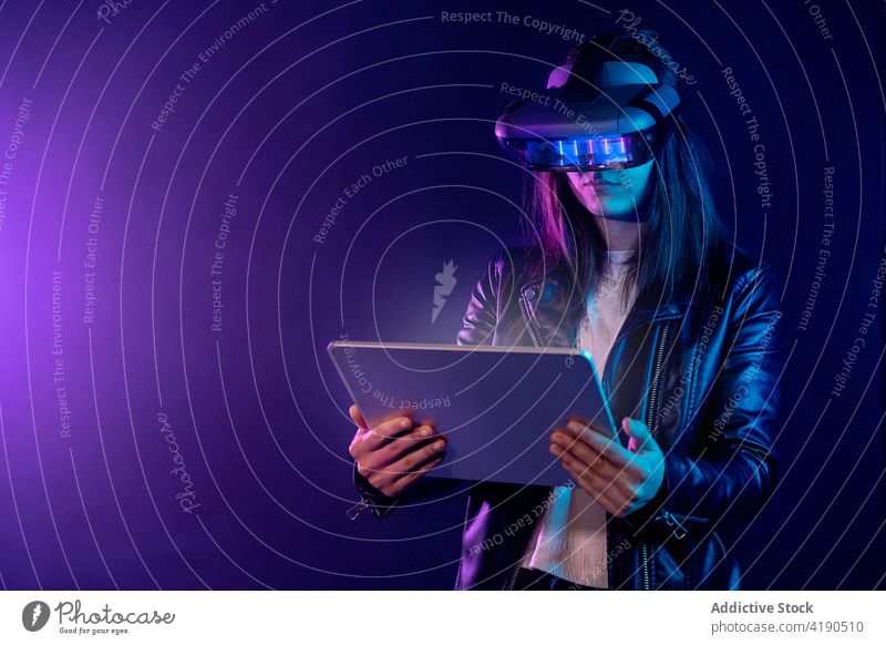 Unrecognizable woman in VR glasses browsing tablet vr goggles headset neon virtual reality cyberspace experience technology illuminate simulate explore device