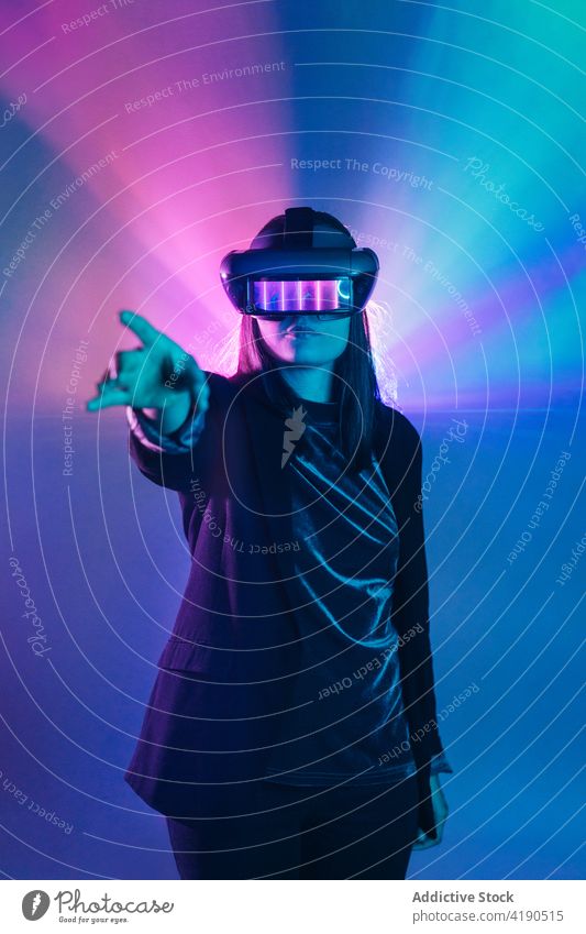 Anonymous woman in VR goggles in neon light vr headset outstretch virtual reality technology cyberspace illuminate simulate experience explore device projector