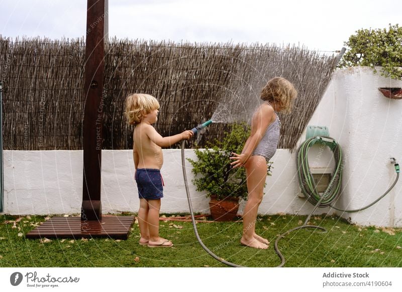 Adorable little siblings playing with water hose in backyard children having fun pour together childhood happy cheerful activity kid toddler sister brother