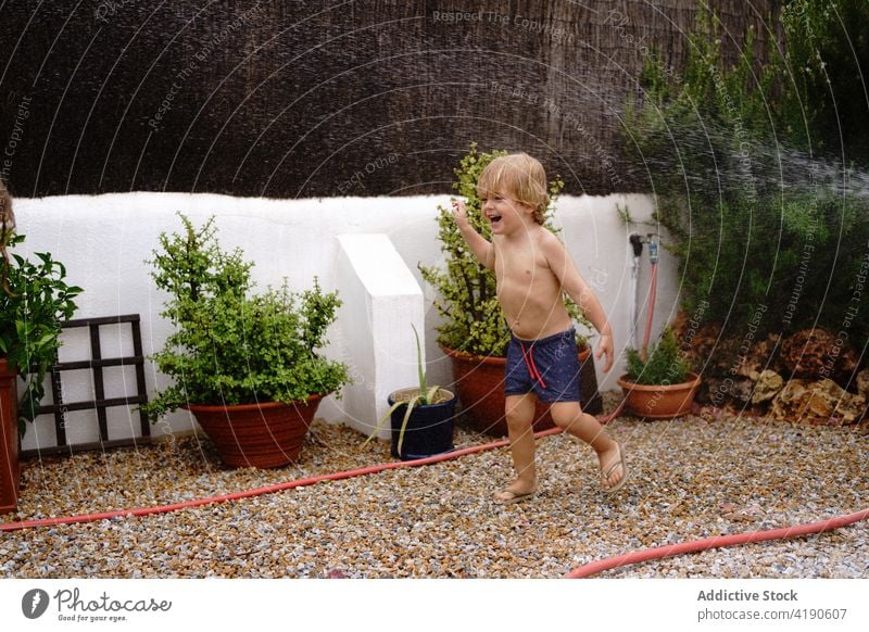 Focused kid watering grassy lawn in backyard child walk focus hose holiday childhood play idyllic vacation happy summer countryside boy swimsuit cultivate