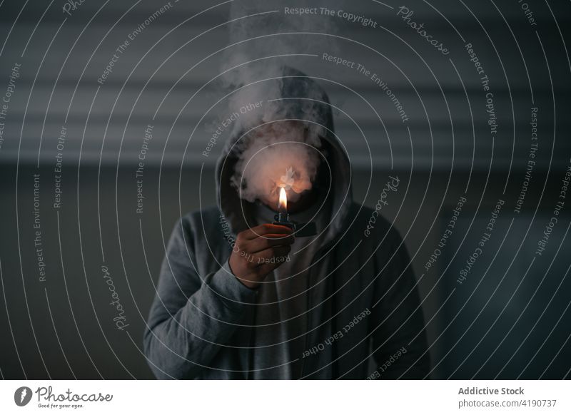 Anonymous man lighting cigarette in darkness smoke lighter fume addict habit tobacco smoker burn nicotine incognito male hoodie jacket inhale flame fire bad