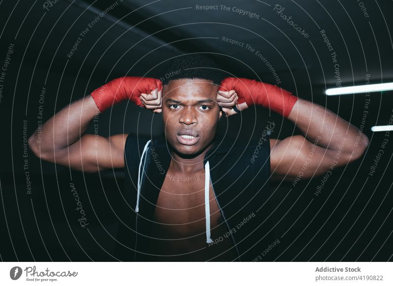 Powerful black boxer looking at camera during training sport workout exercise practice strong power man portrait masculine building hand wrap tape muscular
