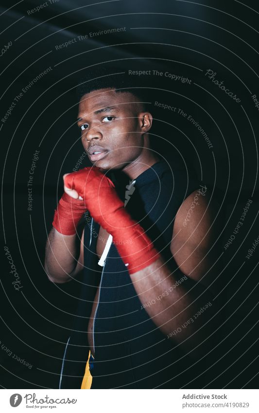 Powerful black boxer looking at camera during training sport workout exercise practice strong power man portrait masculine building hand wrap tape muscular