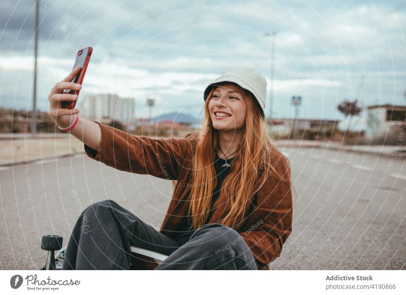 Content young lady sitting on skateboard and taking selfie in countryside woman smile smartphone delight style social media joy millennial mobile female teen