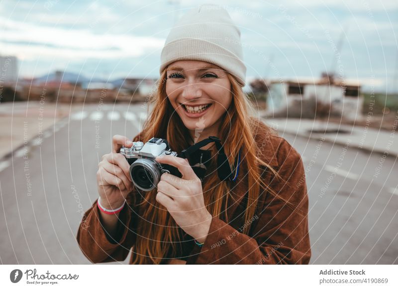 Cheerful young female photographer smiling while standing on road in countryside woman take photo smile positive tourist trip vintage having fun humor long hair