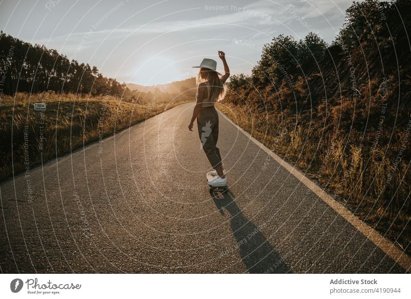Stylish woman skating on empty rural road skater ride cruiser style active energy skateboard balance roadway asphalt young casual summer nature activity sporty