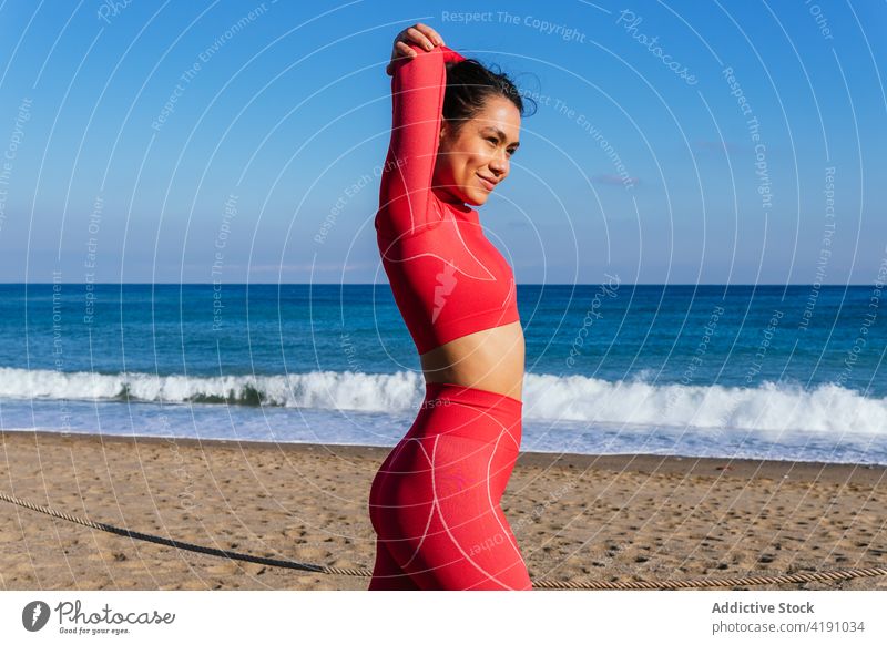 Positive young Hispanic woman warming up on sandy seashore before workout warm up stretch beach ocean training self assured athlete healthy wellness wellbeing