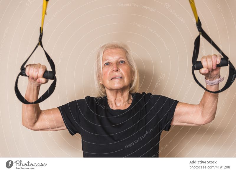 Senior sportswoman exercising with straps on light background athlete suspension training workout practice healthy lifestyle exercise portrait gym loop