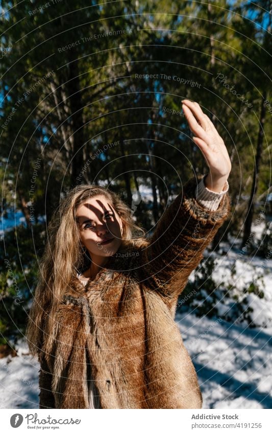 Woman covering face from sun in snowy forest woman winter cover face sunny sunlight wintertime stroll shade woods female shadow fur coat warm warm clothes cold
