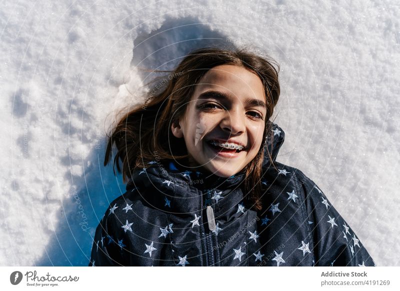 Cheerful girl lying on snow in winter carefree cheerful teenage braces candid smile jacket warm happy cold content delight outerwear season enjoy ground