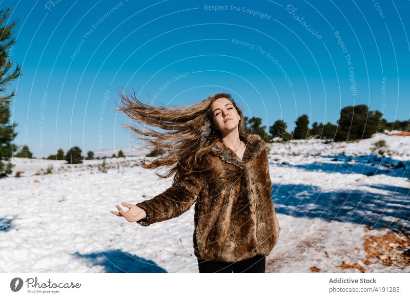 Carefree woman playing with hair in winter forest carefree flying hair wave hair meadow snow sunny enjoy female freedom fur coat warm weather warm clothes