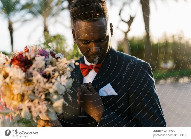 Stylish black groom with flowers in garden bouquet adjust newlywed style elegant suit wedding male man african american ethnic bunch event ceremony summer