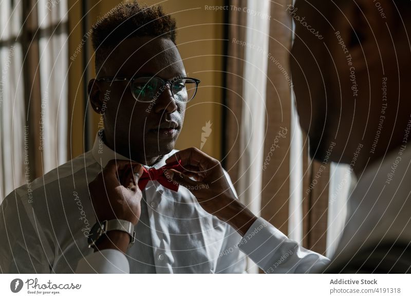 Ethnic brothers in classy outfits in room on wedding day groom adjust bow tie best man help friend newlywed fiance ethnic black african american ceremony men