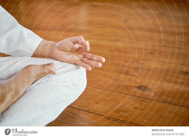 Crop man meditating while showing mudra gesture in room yoga practice spirit meditation harmony wellness meditate white cloth parquet serene energy vitality