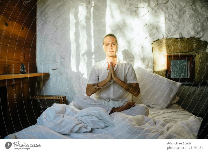 Blond man sitting on a bed while practicing meditation blond bedroom yoga stretch flexibility wellness health exercise sportswear people lifestyle workout