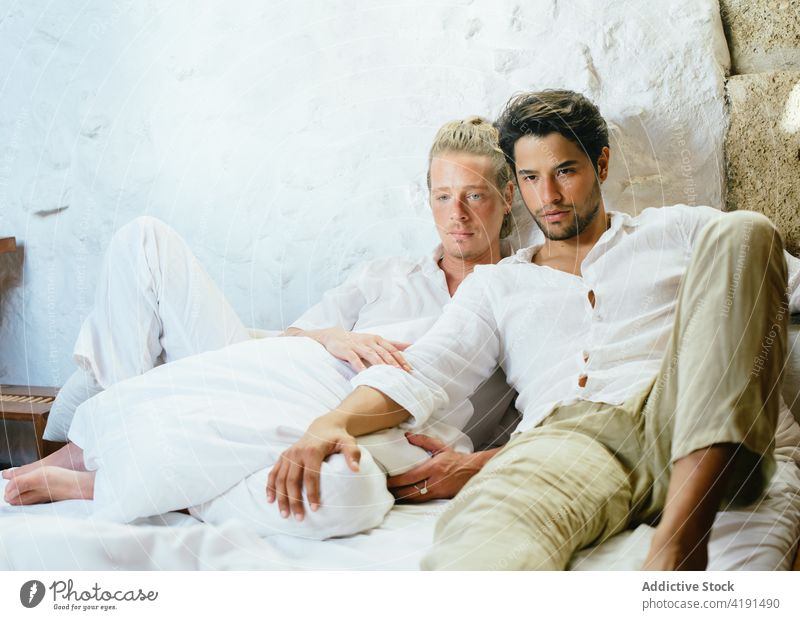 Two men sitting on the bed looking away relationship homosexual male couple home bedroom love young together affection boyfriend adult romantic gay lifestyle