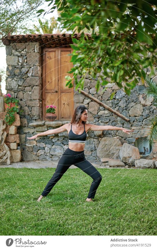 Woman demonstrating warrior two pose in garden woman yoga healthy lifestyle flexible Virabhadrasana stretch balance practice lawn courtyard wellness natural