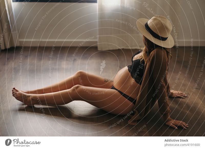 Anonymous pregnant woman sitting on floor anonymous pensive pregnancy relaxed maternal expect resting chilling style female mother touch belly hat prenatal joy