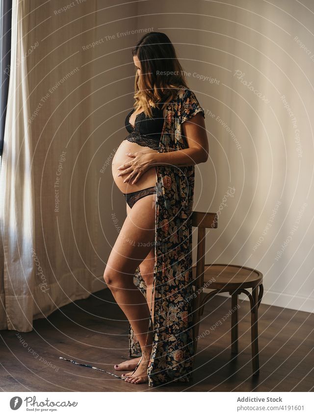 Pregnant woman touching belly and looking down pregnant anonymous style touch belly motherhood prenatal expect apartment lingerie female hat parenthood dreamy
