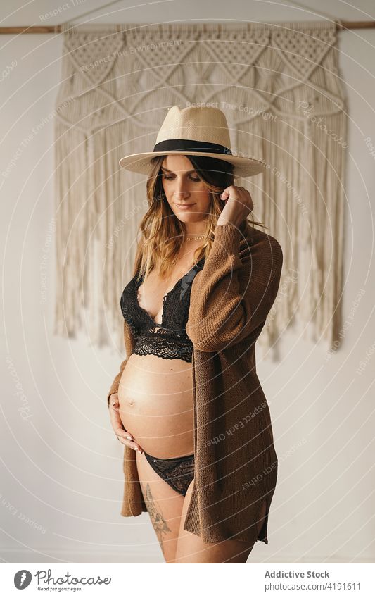 Pregnant woman touching belly and looking down pregnant pensive style touch belly motherhood prenatal expect apartment lingerie female hat parenthood dreamy