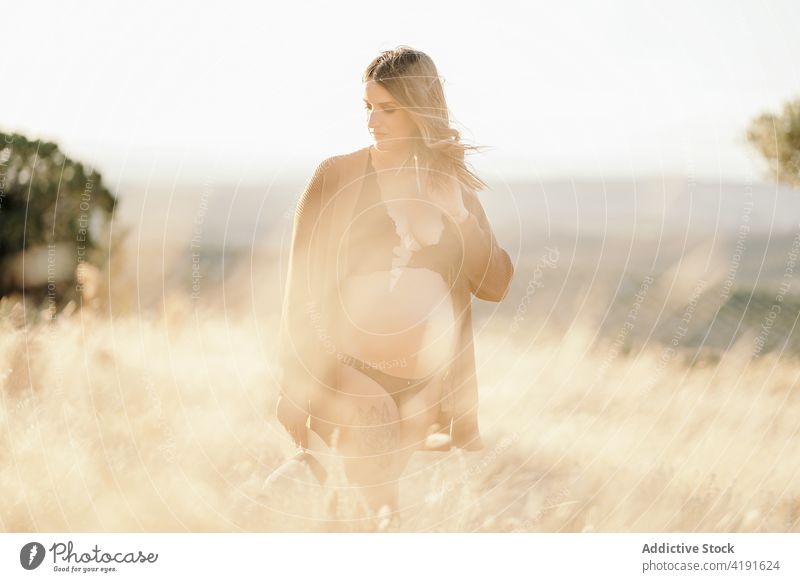 Pregnant female standing in field in countryside woman pregnant nature pensive maternal environment mother peaceful lingerie calm daytime expect tranquil sun