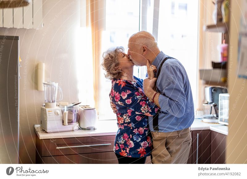 Happy senior couple kissing in the kitchen real people candid genuine woman mature female together love bonding Caucasian elderly home house old aging