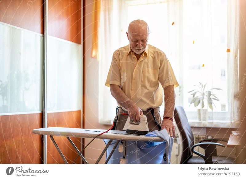 Senior man at home ironing his clothes real people candid genuine senior mature male Caucasian elderly house old aging domestic life grandfather pensioner