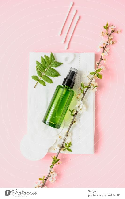 A green perfume bottle and cosmetics on a pink background. Flatl lay. Spring. Perfume Bottle cosmetic products Cotton bud cotton pads Flowering plant flatlay