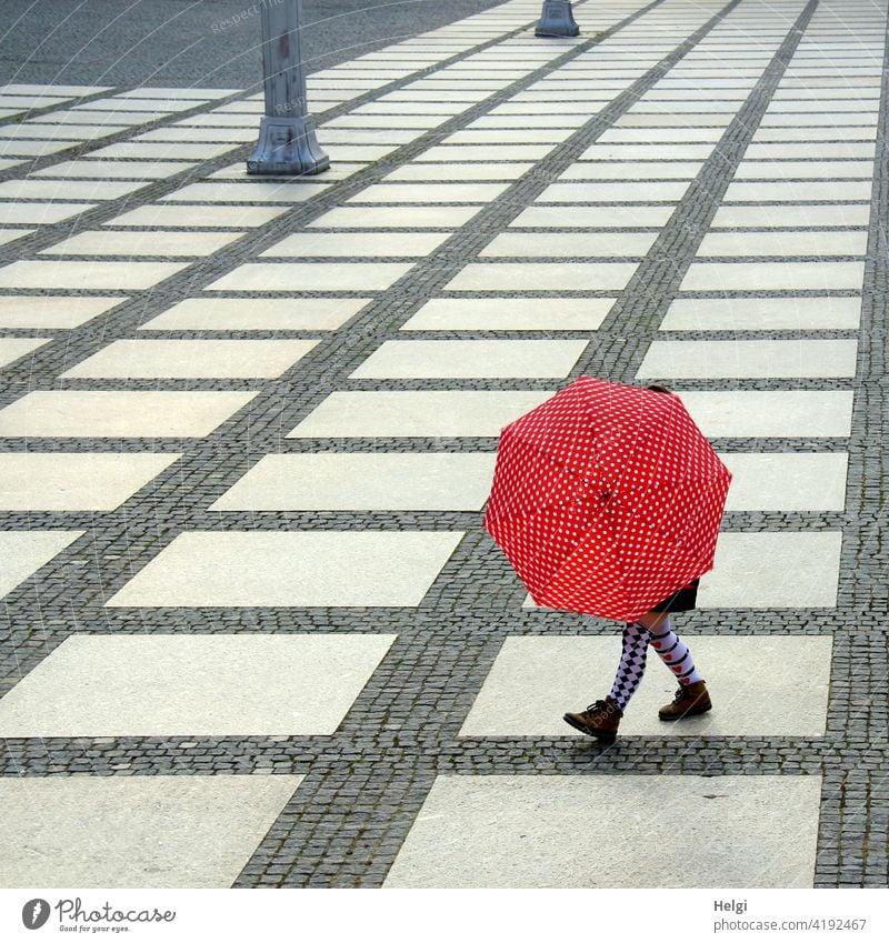 Woman with colorful stockings behind a red and white dotted umbrella on a large square with graphic pavement Human being Legs Stockings Footwear variegated