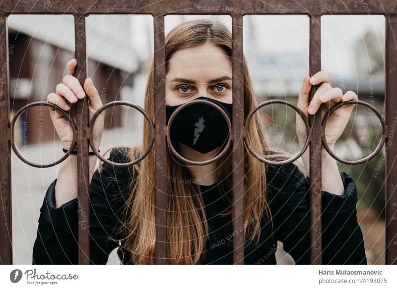 woman with face mask behind the bars outdoors, concept lockdown covid 19 adult alone cage corona corona virus coronavirus covid lockdown covid-19 depressed